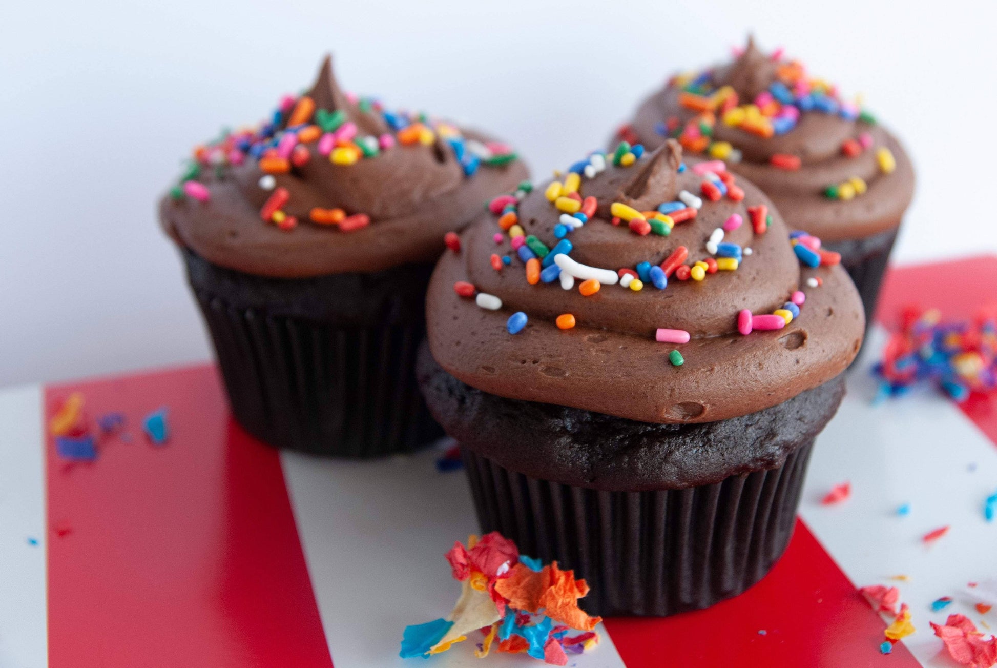 Chocolate cupcakes with colorful sprinkles on a red surface