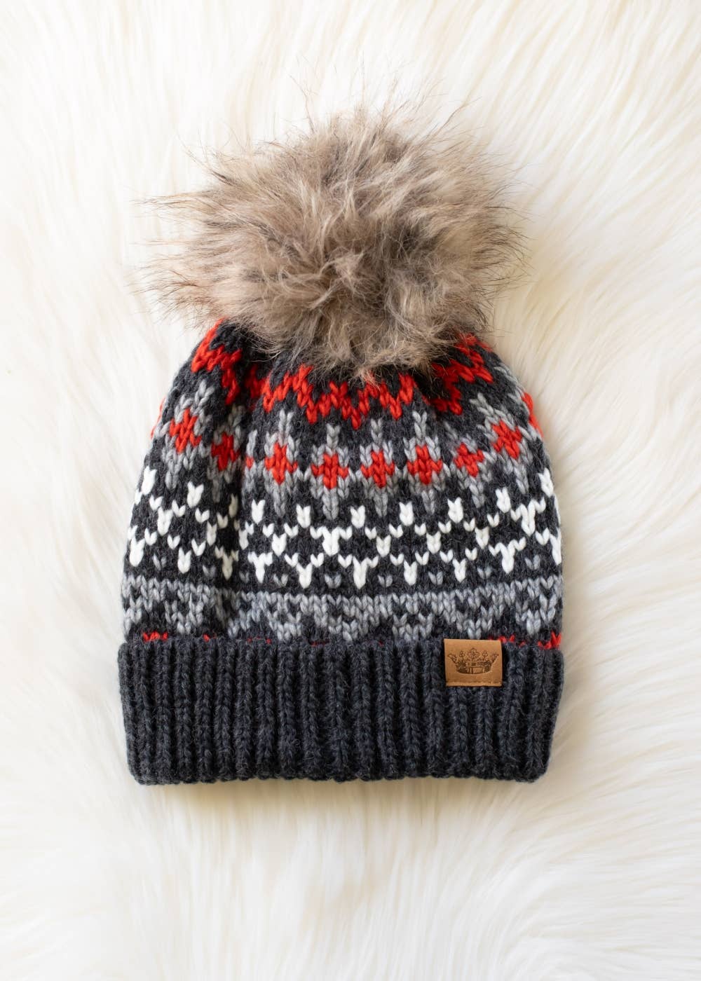 Knitted beanie with a fur pom-pom on a white textured background