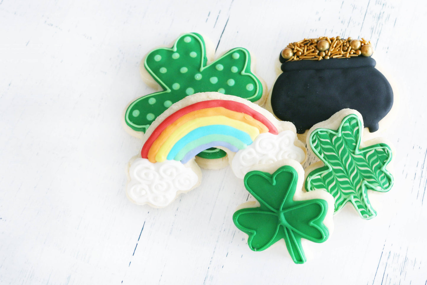 Decorative cookies shaped like a rainbow, pot of gold, and shamrocks on a white background