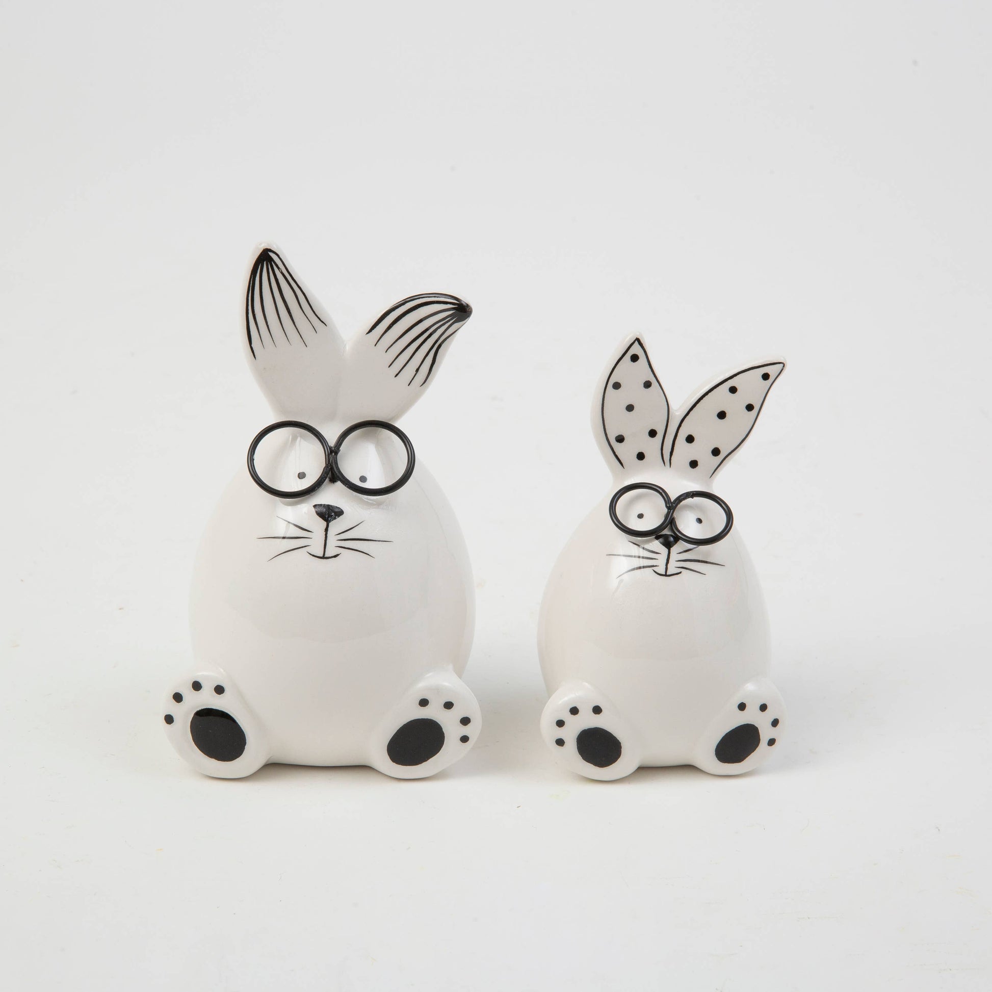 Two white ceramic rabbit figures with black details on a white background