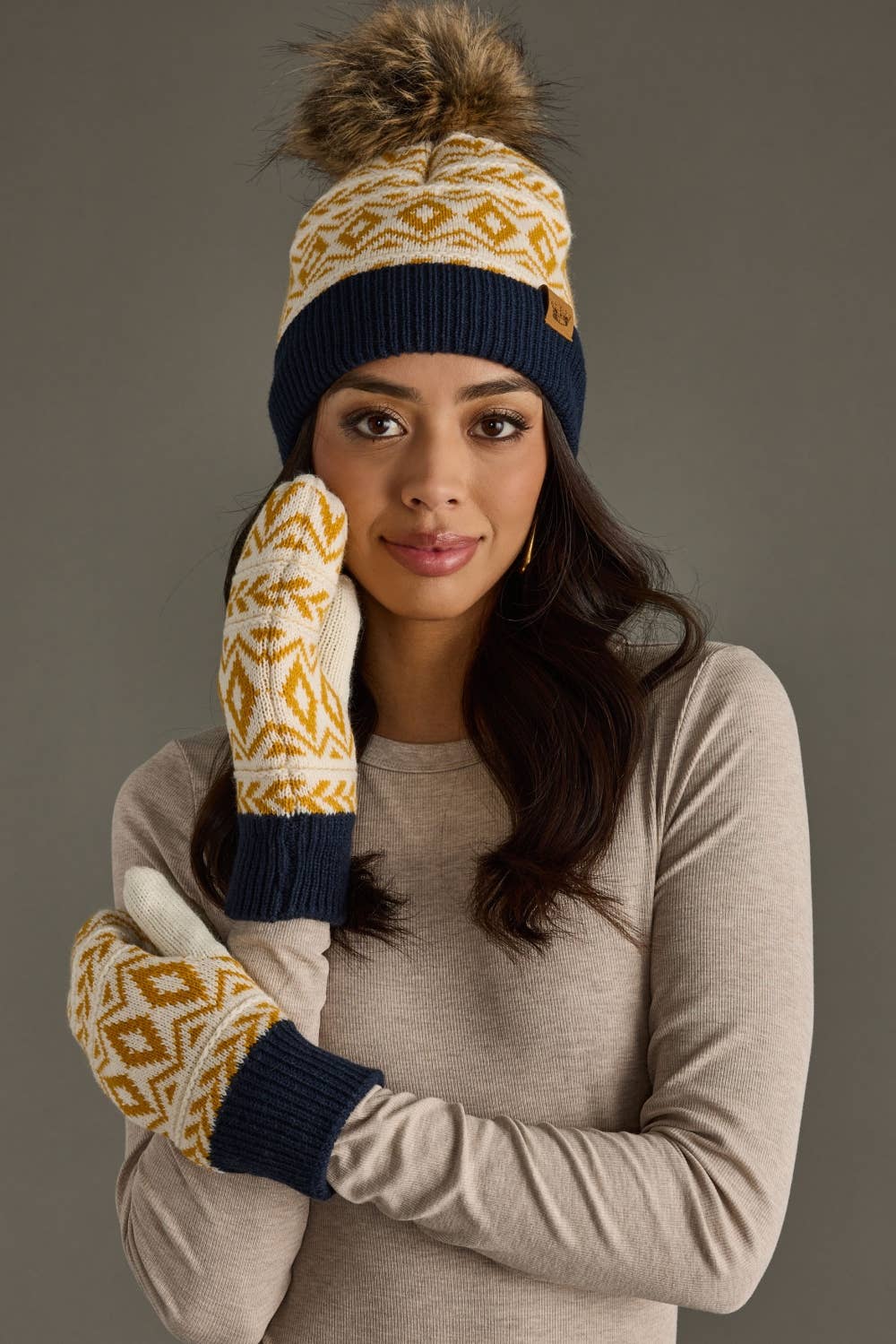 Woman wearing a patterned beanie and mittens against a gray background