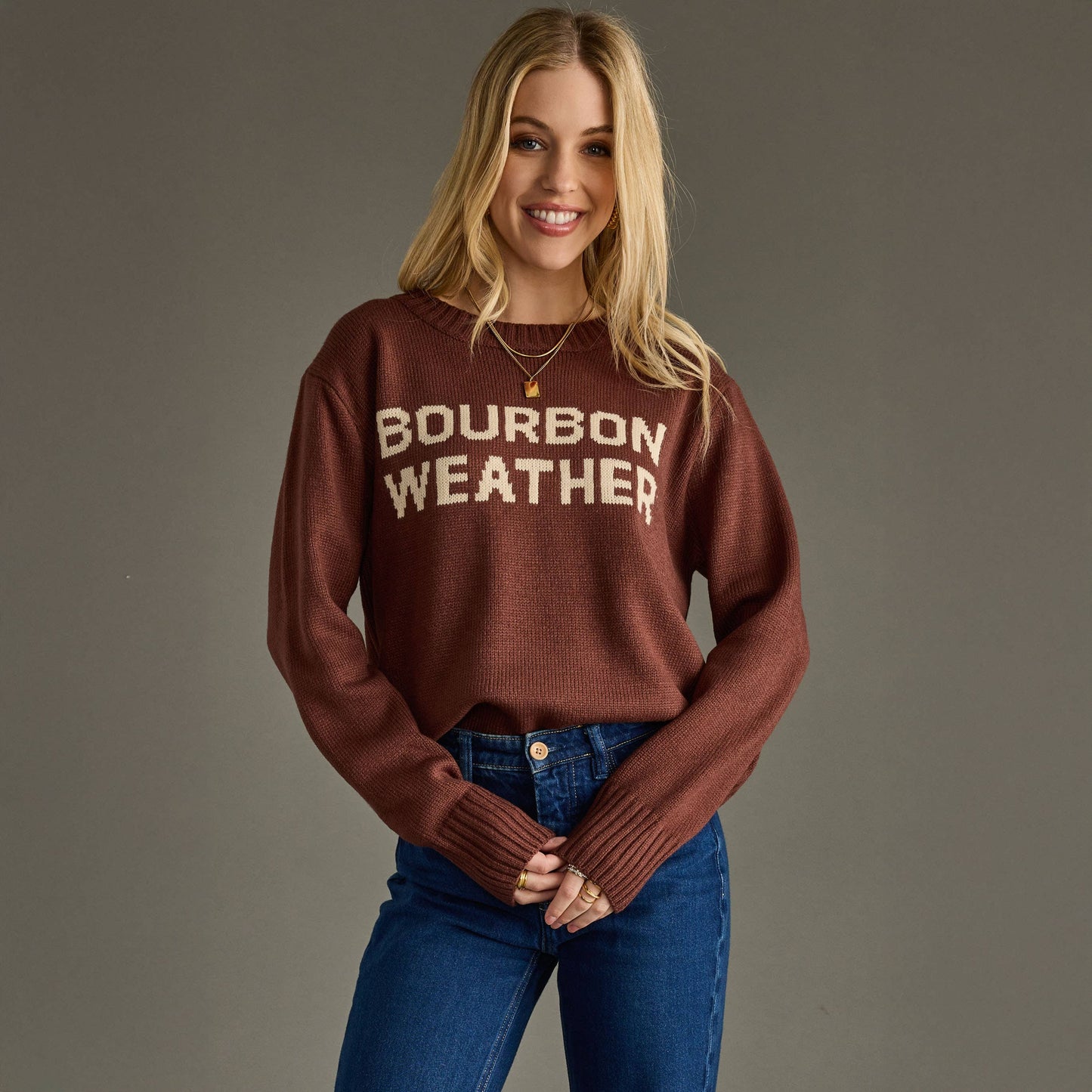 Woman wearing a brown sweater with 'Bourbon Weather' text against a gray background