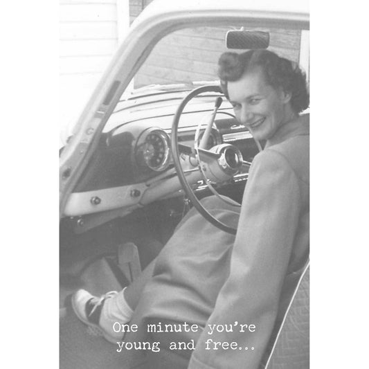 Black and white photo of a woman sitting in an old car with a steering wheel.