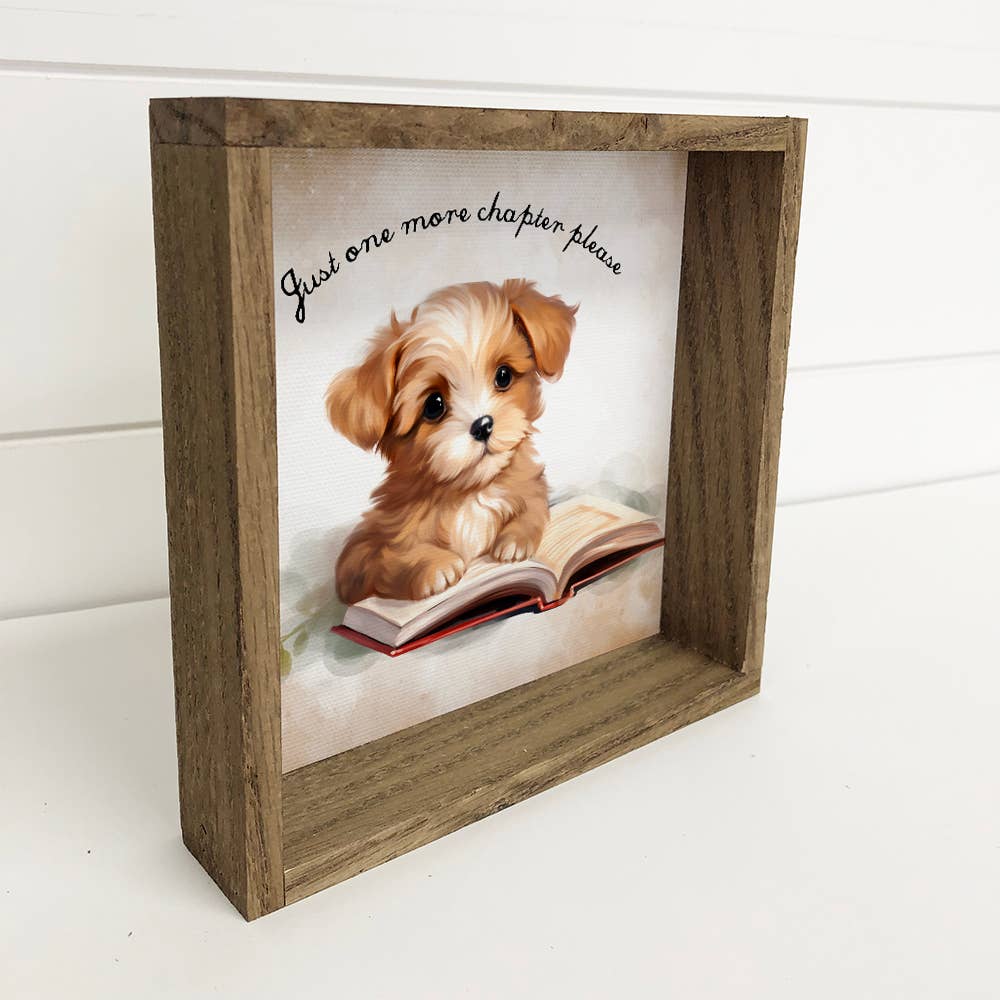 Wooden framed picture of a puppy on a book with text 'Just one more chapter please' on a white background.