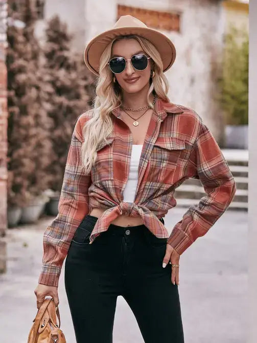 Woman wearing a plaid shirt, black pants, and a hat outdoors.