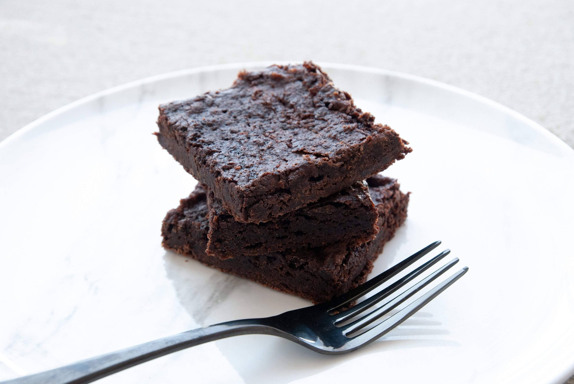 Two brownies stacked on a white plate with a fork beside them.