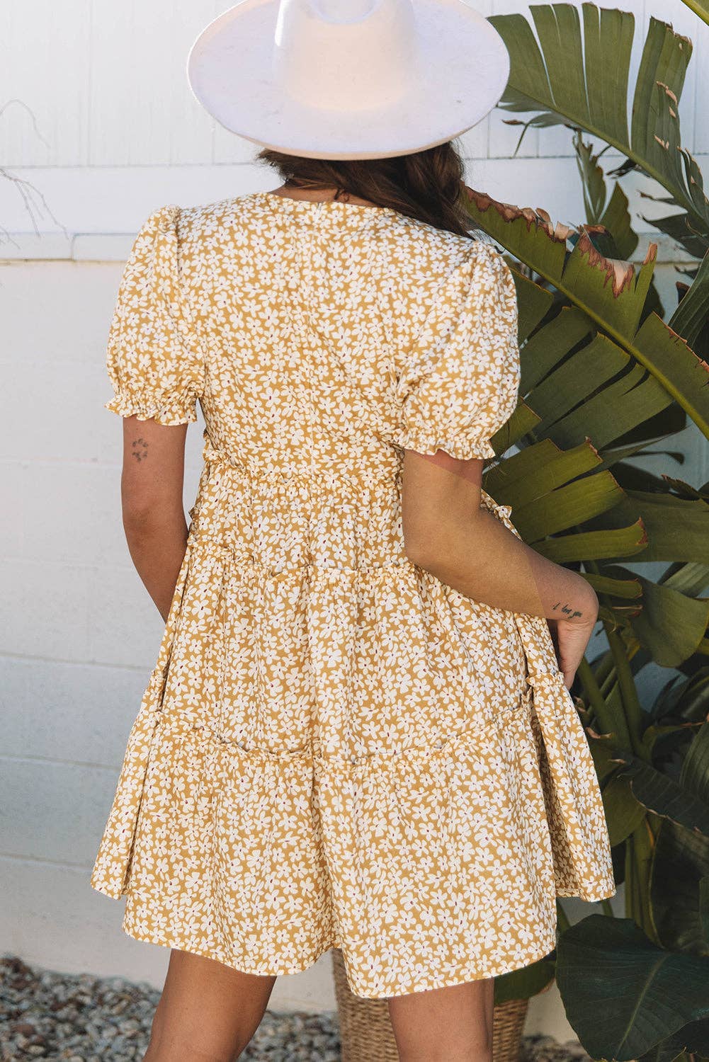 Person wearing a yellow floral dress with puffed sleeves, standing next to a plant.