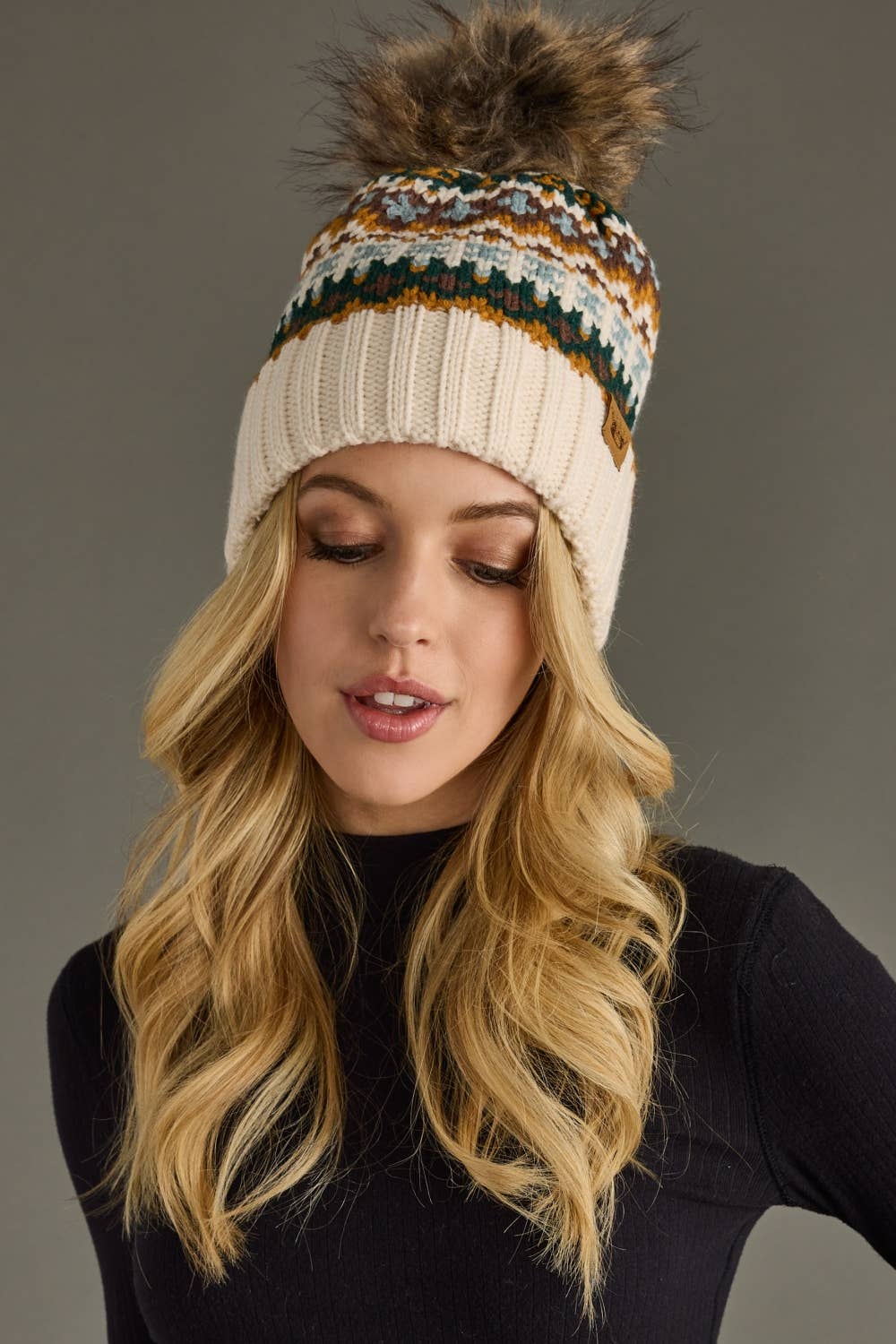 Woman wearing a patterned knit beanie with a pom-pom on a gray background