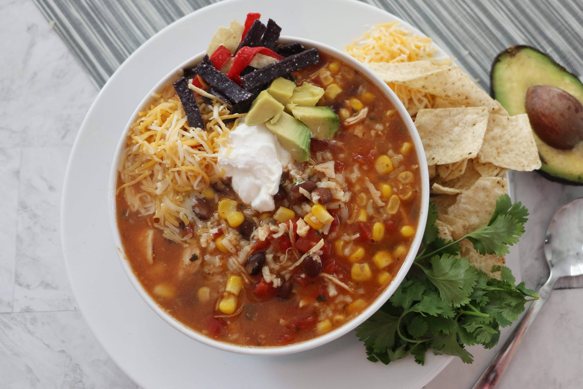 Tortilla soup with toppings on a white plate on a gray surface