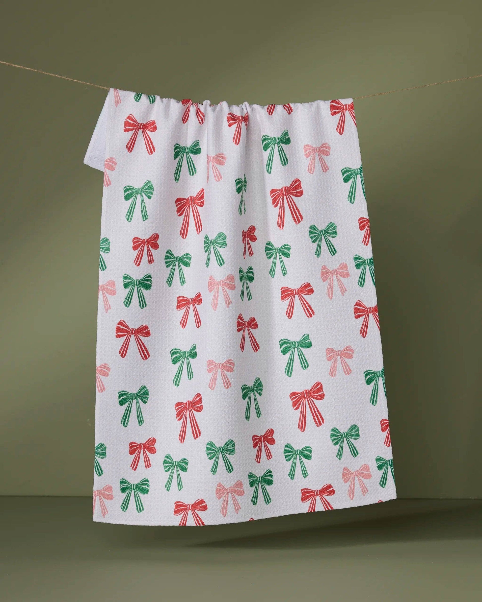 Geometry Tea Towel with red and green bow pattern hanging on a line against a green background
