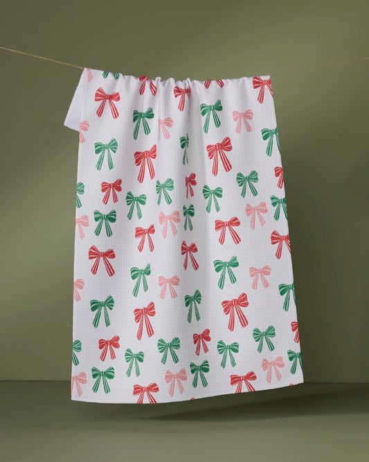 Geometry Tea Towel with red and green bow pattern hanging on a line against a green background