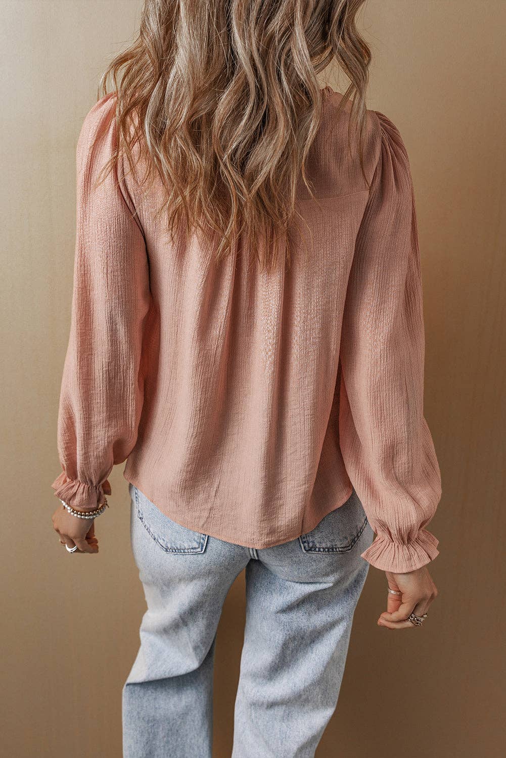Person wearing a pink blouse with long sleeves and light blue jeans against a beige background