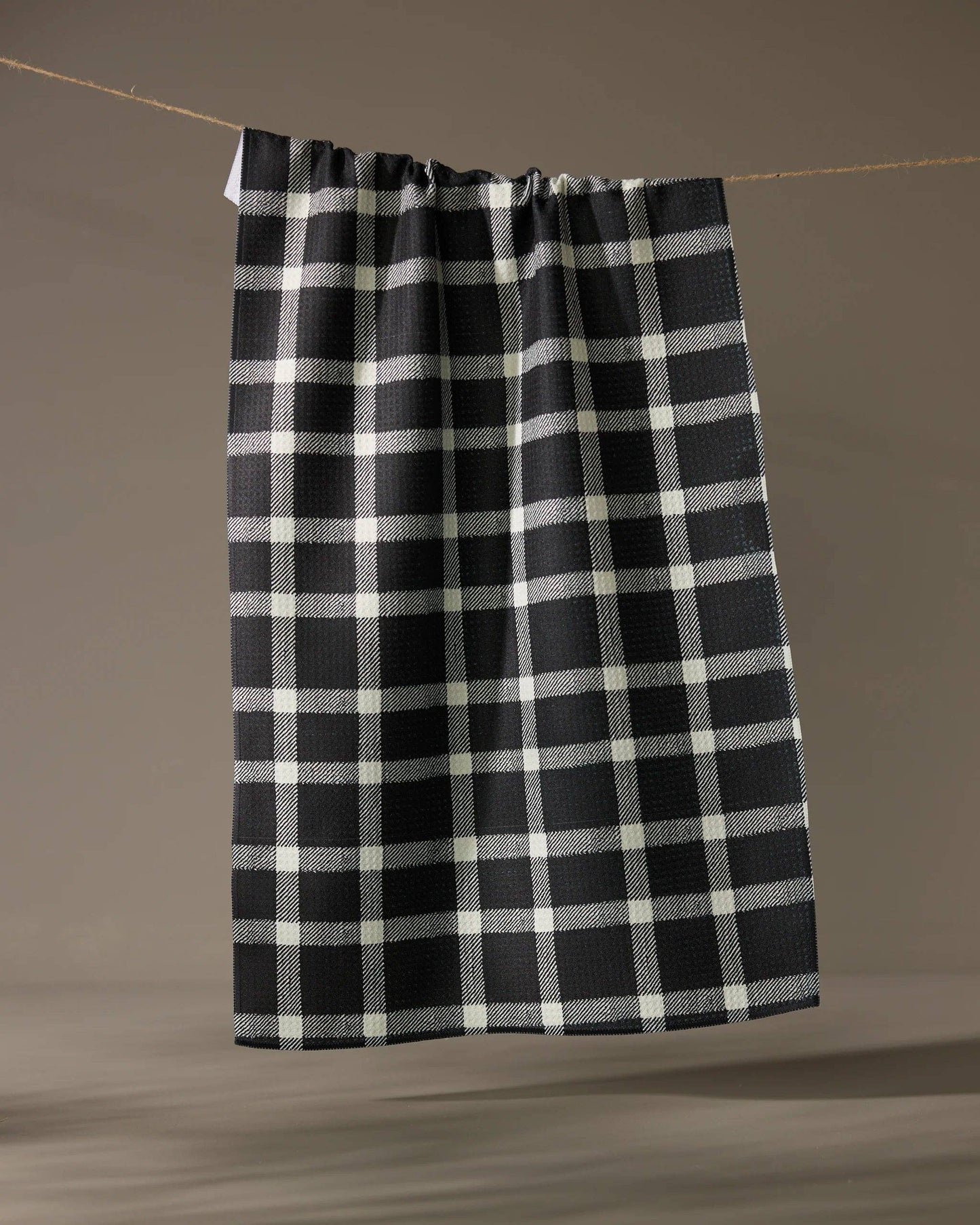 Geometry Tea Towel Black and white checkered towel hanging on a line against a brown background