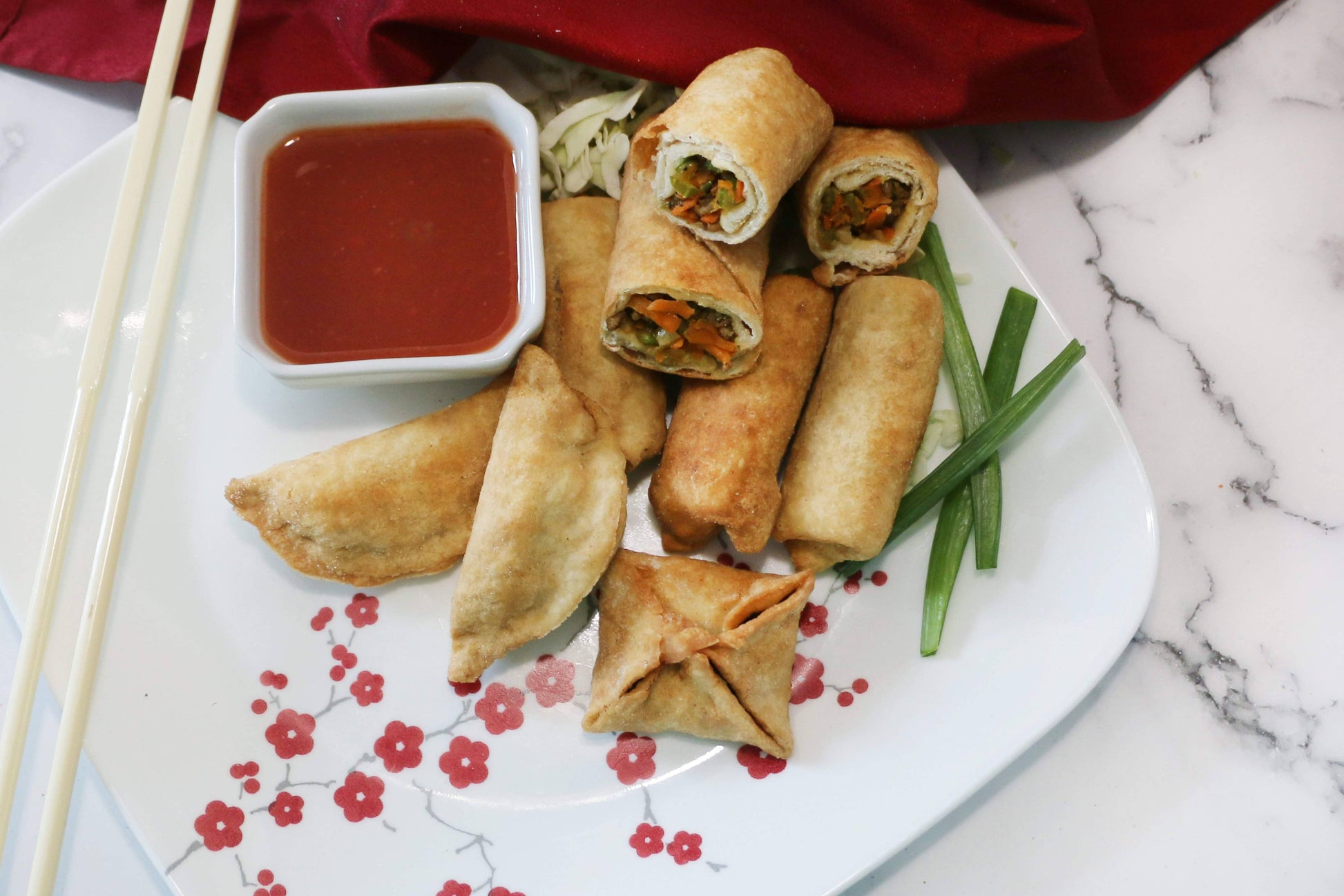 Plated spring rolls with dipping sauce and green beans on a floral plate.