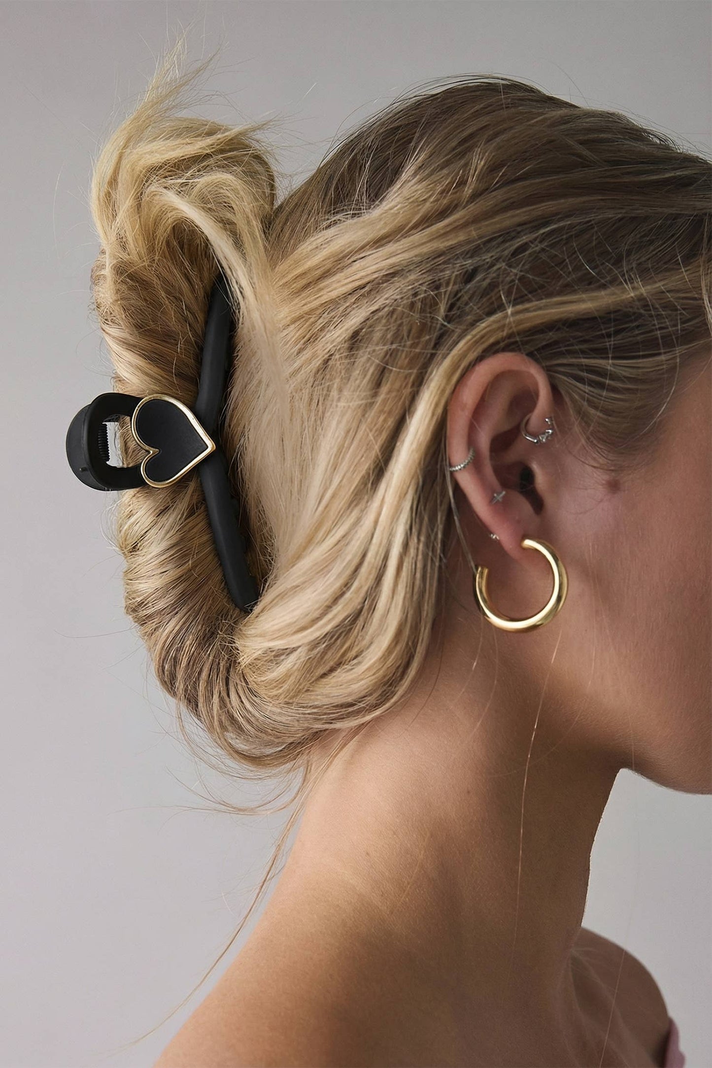 Close-up of a person's ear with gold hoop earrings and a black hair clip on a neutral background