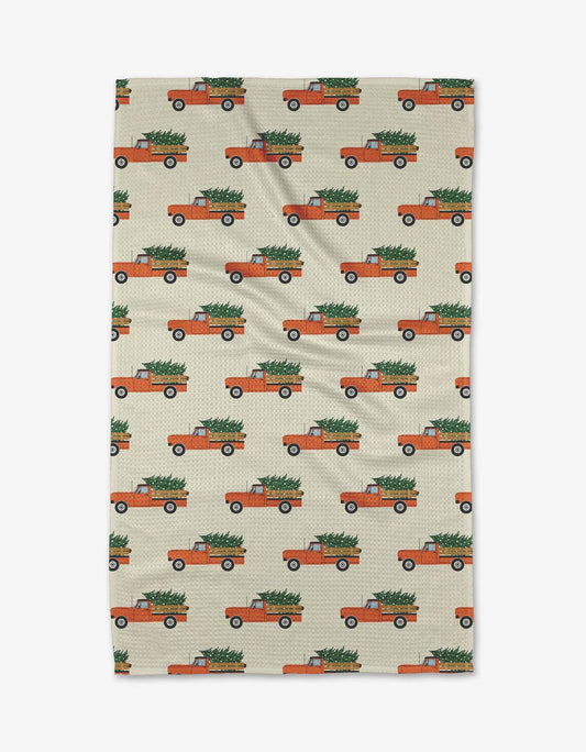 Geometry Tea Towel Christmas Ride Patterned towel with orange trucks carrying Christmas trees on a beige background