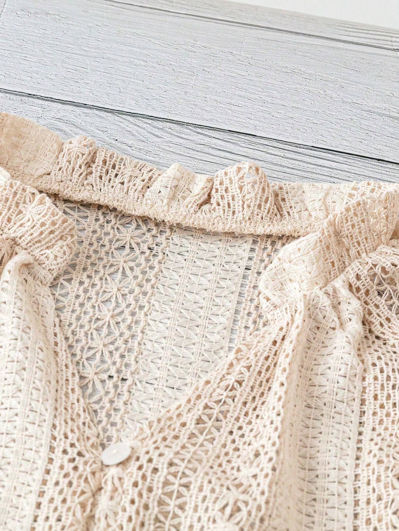 Close-up of a beige knitted garment with lace trim on a light wooden surface.