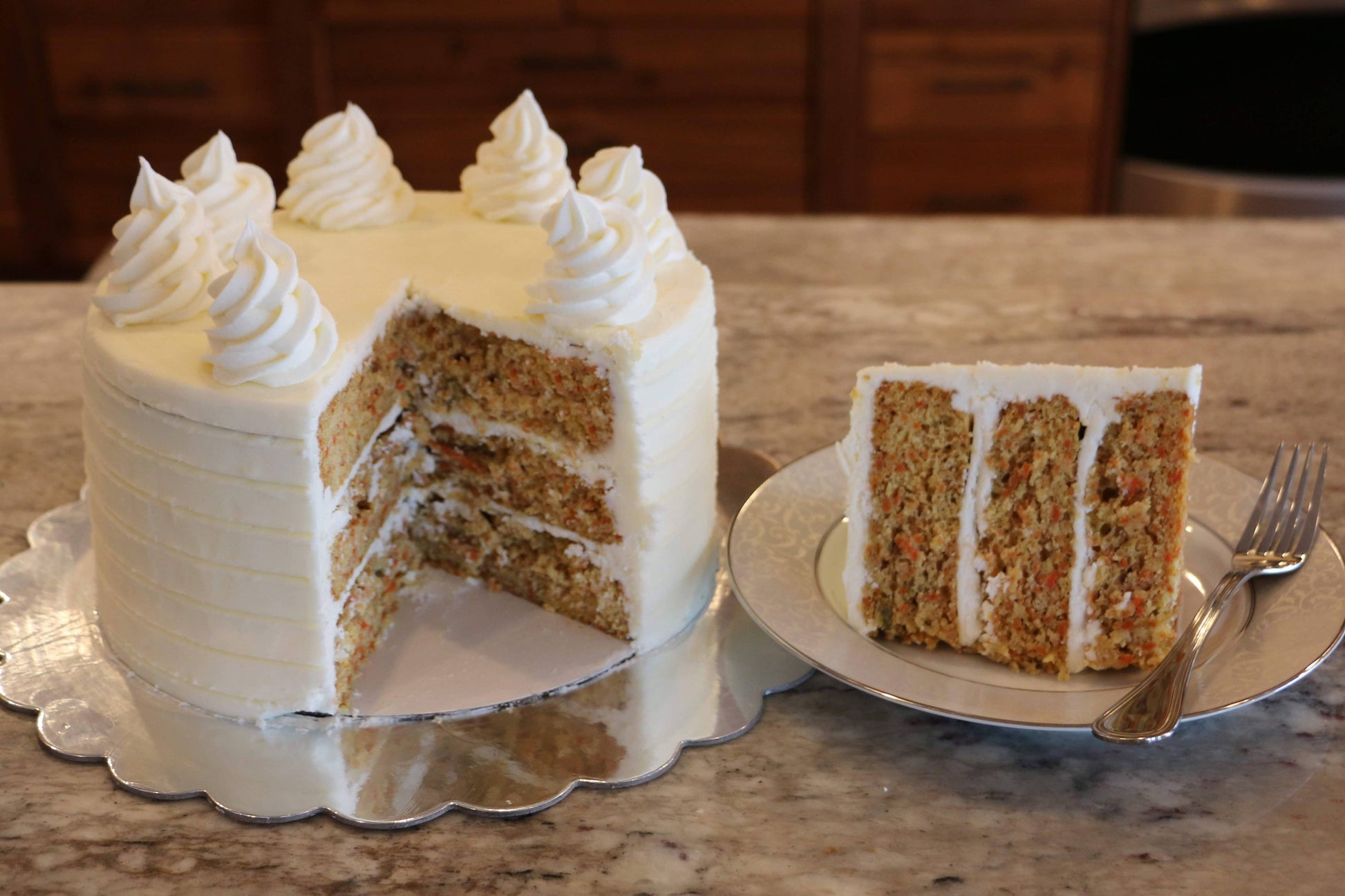 Carrot cake with a slice taken out on a plate, placed on a marble surface.