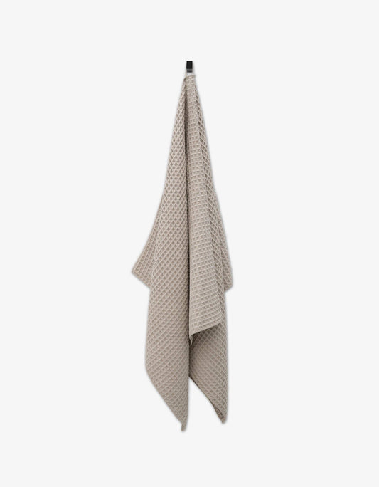 A taupe colored waffle bath towel hanging against a white background.