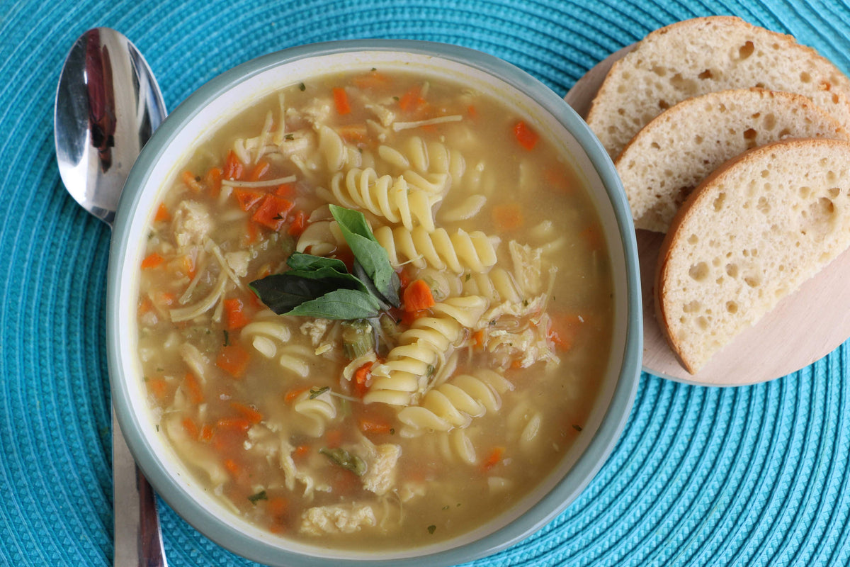  bowl of soup with pasta, carrots, and bread slices on a blue placemat