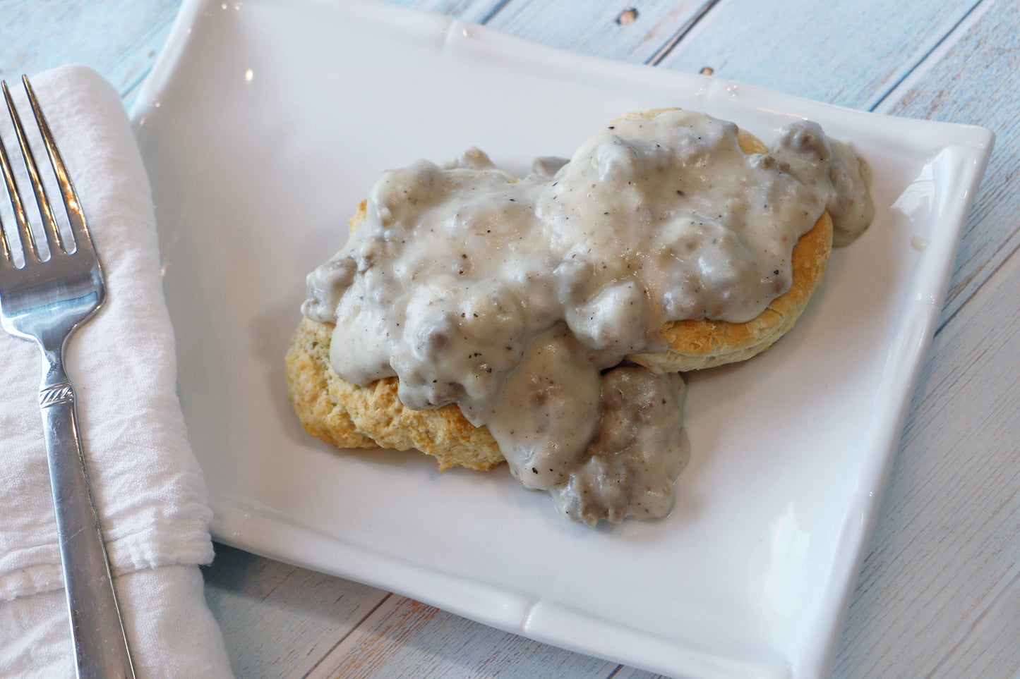 Biscuits with gravy on a white plate with a fork and napkin.