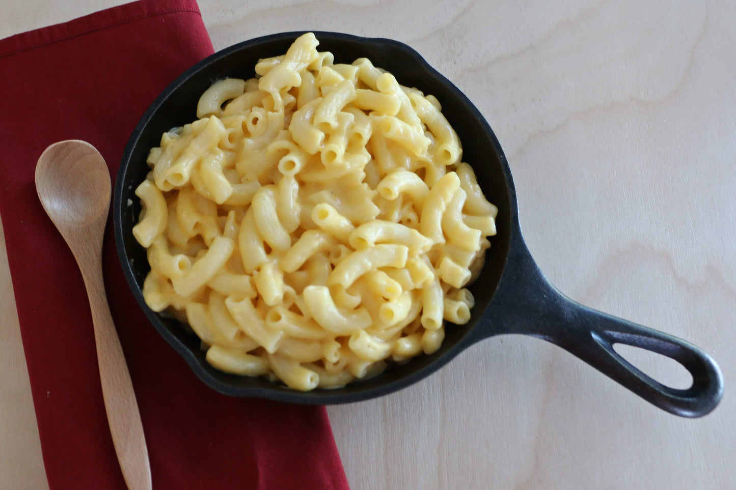 Macaroni and cheese in a black skillet on a red cloth with a wooden spoon.