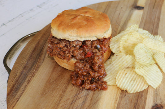 Sloppy joe sandwich on a wooden cutting board with potato chips