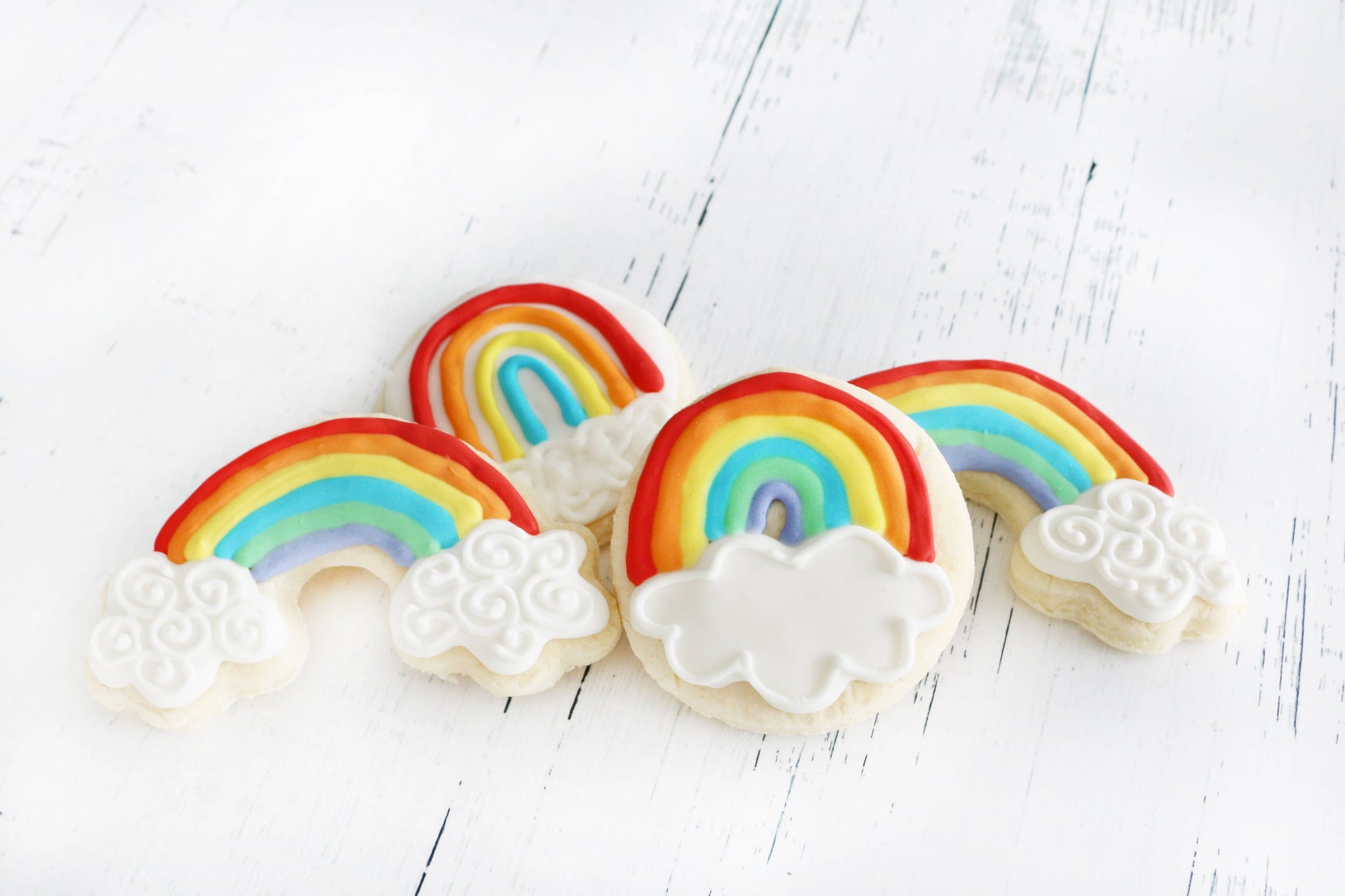 Cookies decorated with rainbow and cloud designs on a white wooden surface