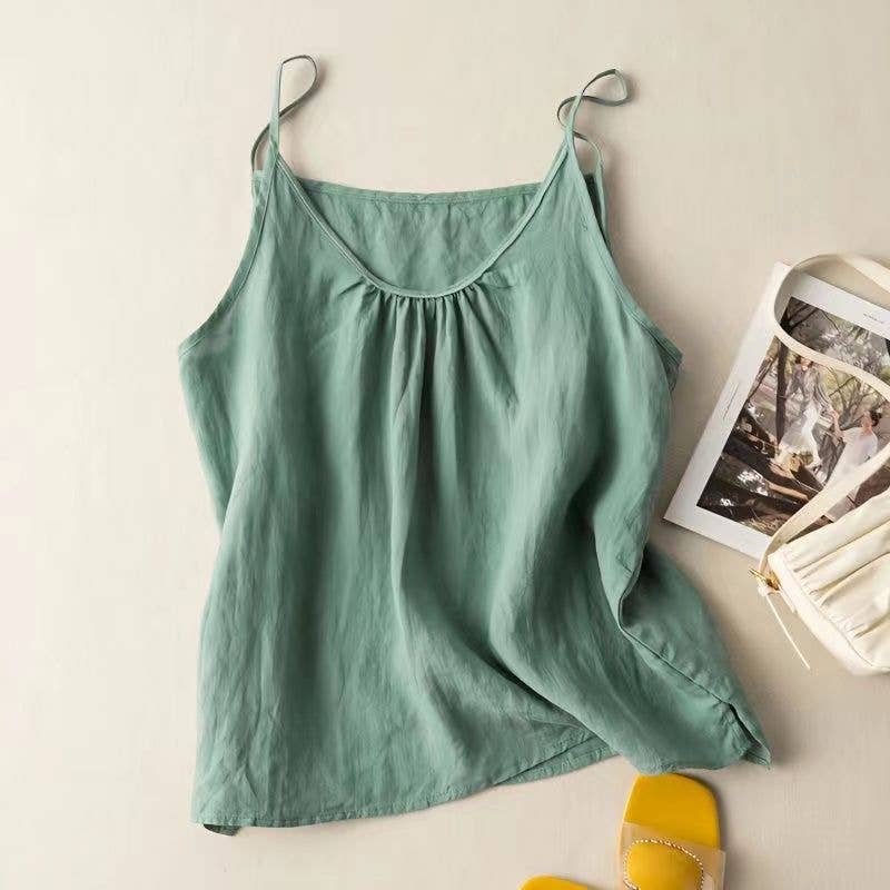 Green tank top on a hanger with a magazine and yellow shoes on a light surface