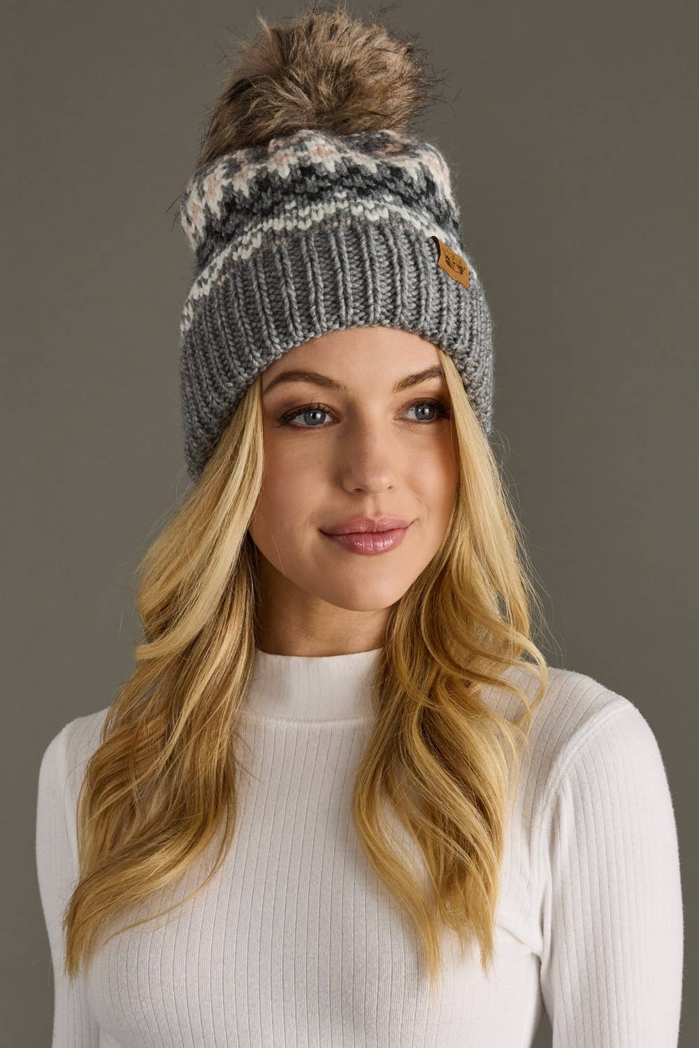 Woman wearing a gray knit beanie with a pom-pom on a gray background