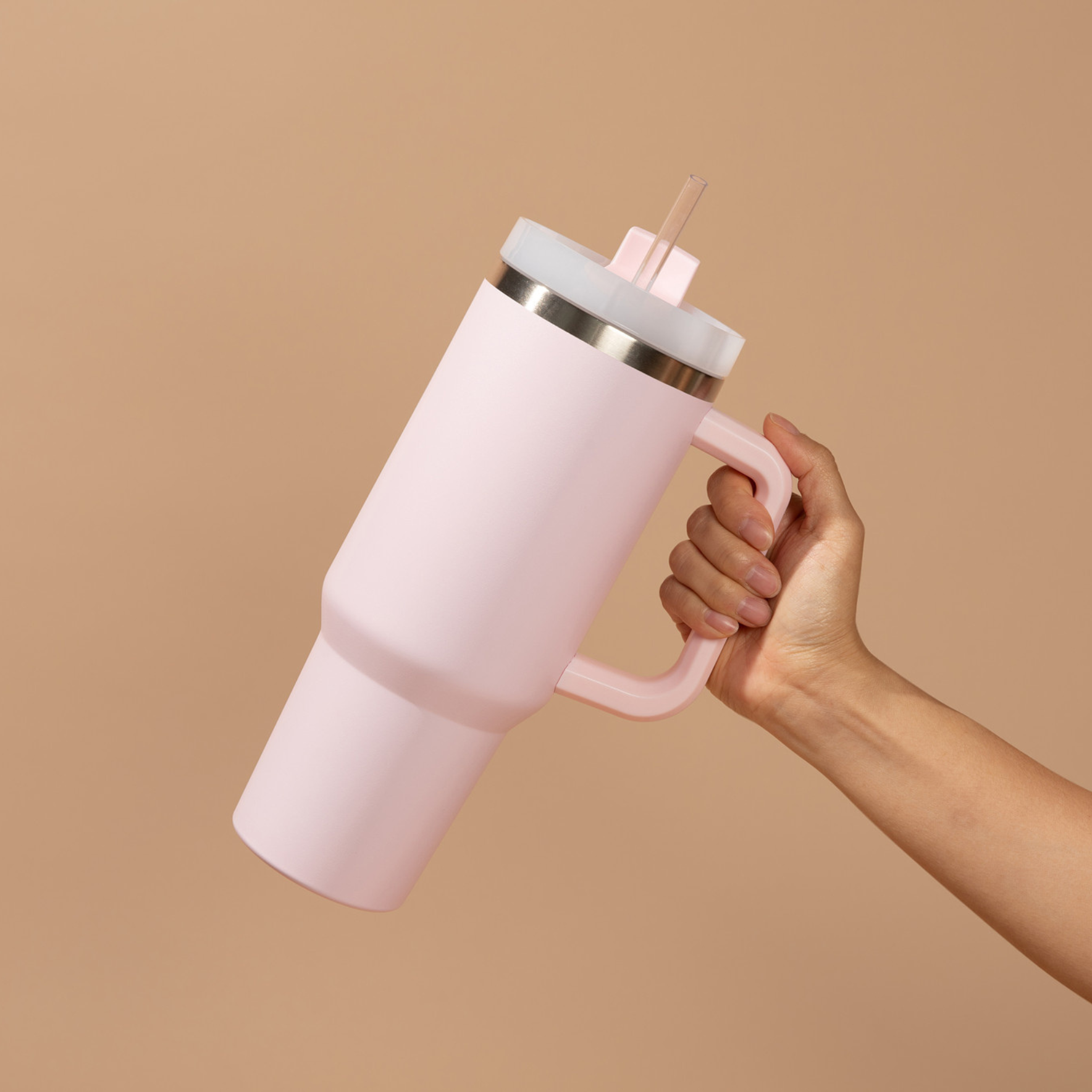 Pink insulated tumbler with a handle held by a hand against a beige background