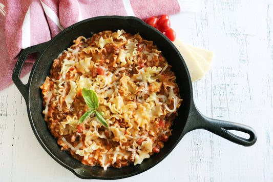 Pasta dish in a black skillet on a white surface with a pink cloth in the background