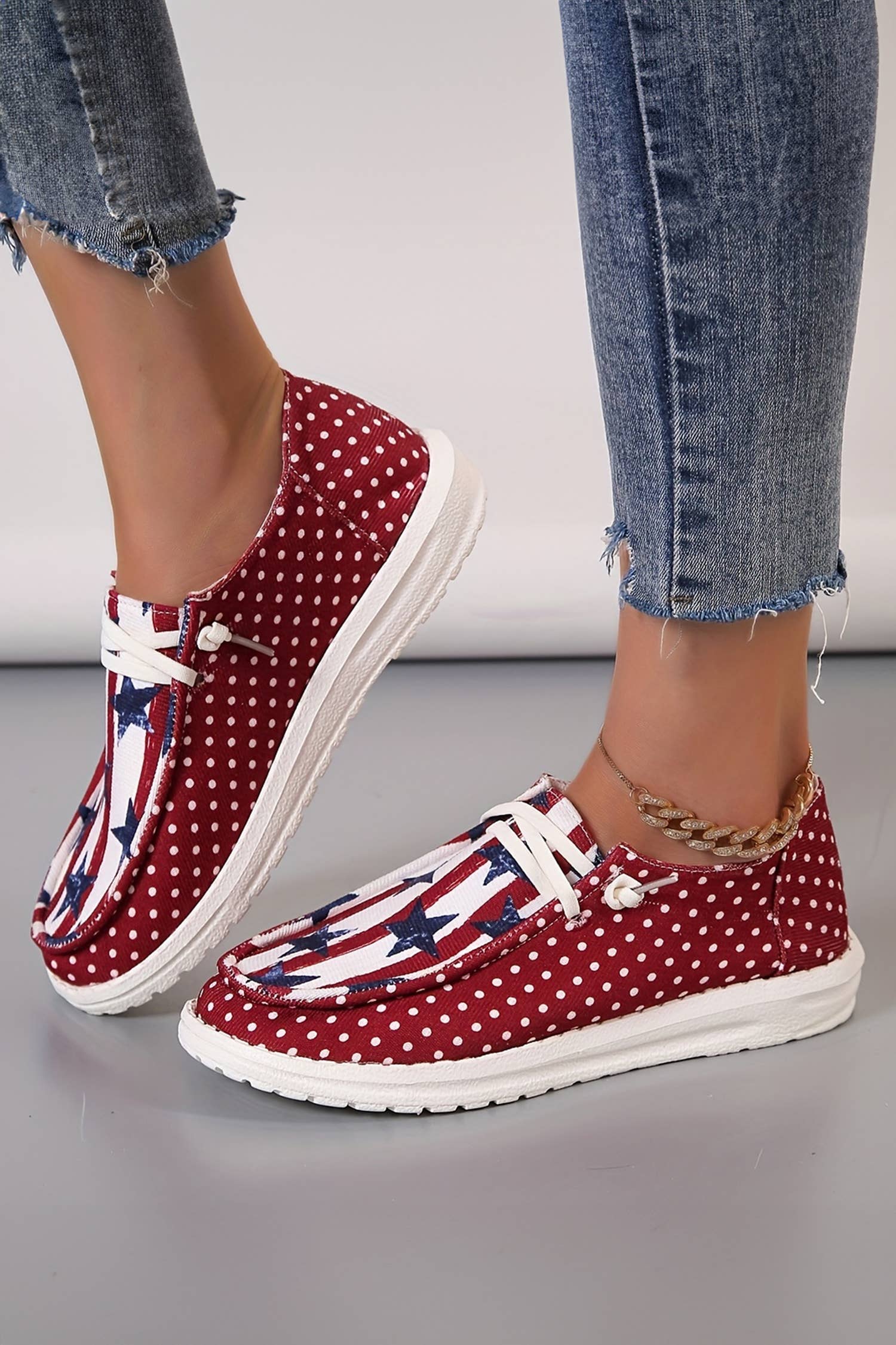 Red polka dot shoes with American flag pattern worn with blue jeans on a light gray background