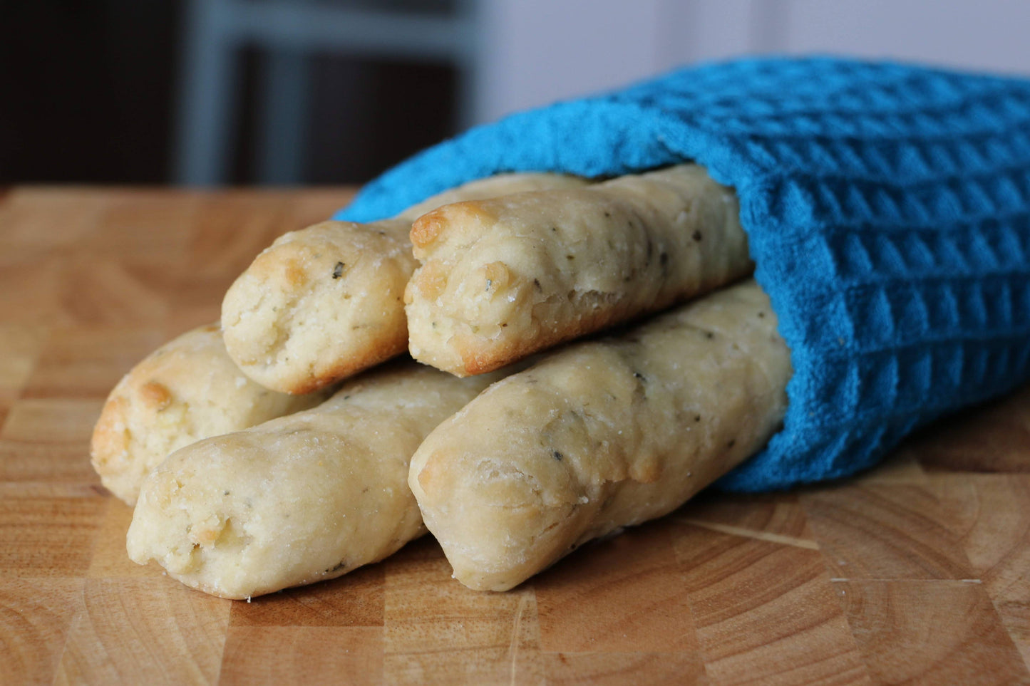 Three bread rolls wrapped in a blue oven mitt on a wooden surface