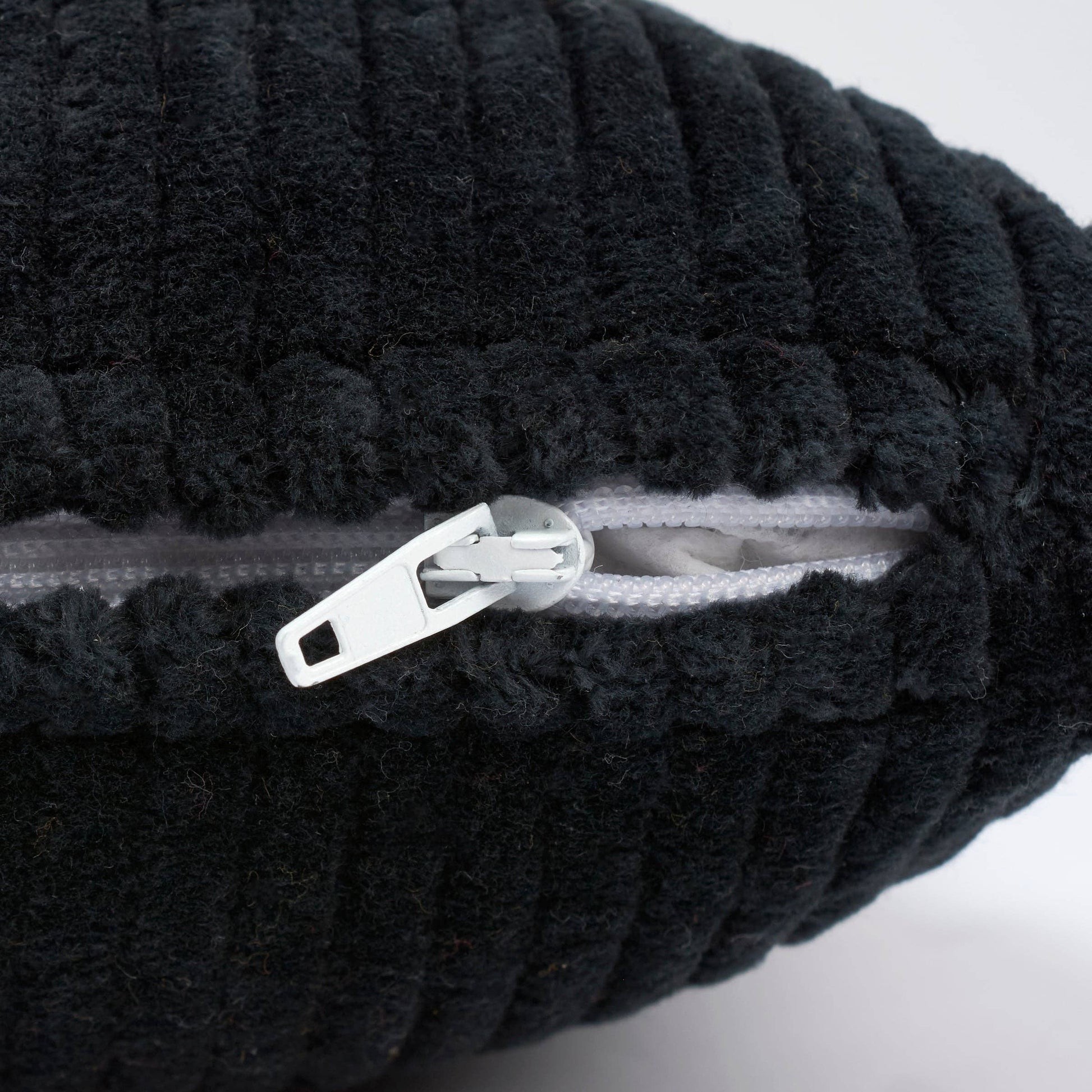 Close-up of a black ribbed plush or bouclé fabric item with a white zipper and white zipper pull, shown against a light neutral background.