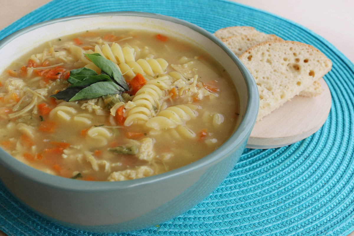 Bowl of pasta soup with bread on a blue textured surface