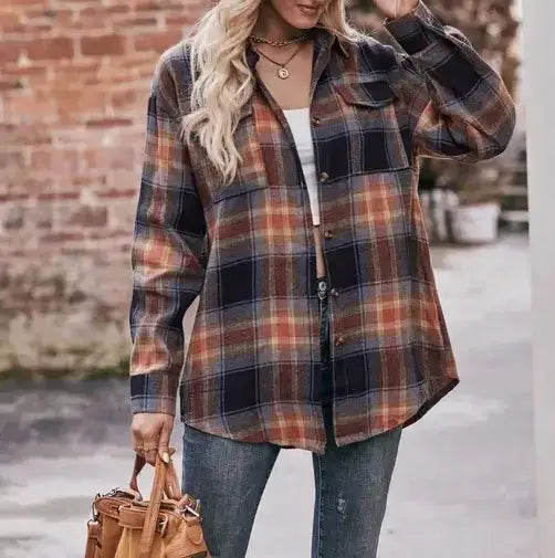 A woman wearing a long-sleeve plaid button-up shirt in brown, orange, and navy tones, paired with a white tank top and blue jeans, holding a brown leather handbag.