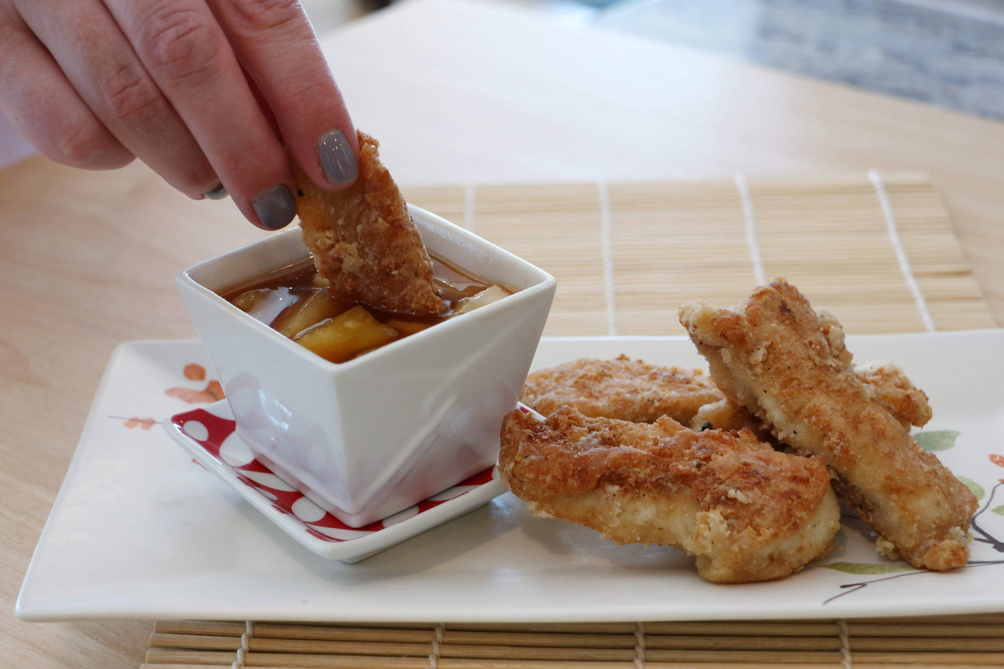 Person dipping a fried chicken strip into a small bowl of sauce on a plate with more chicken strips.