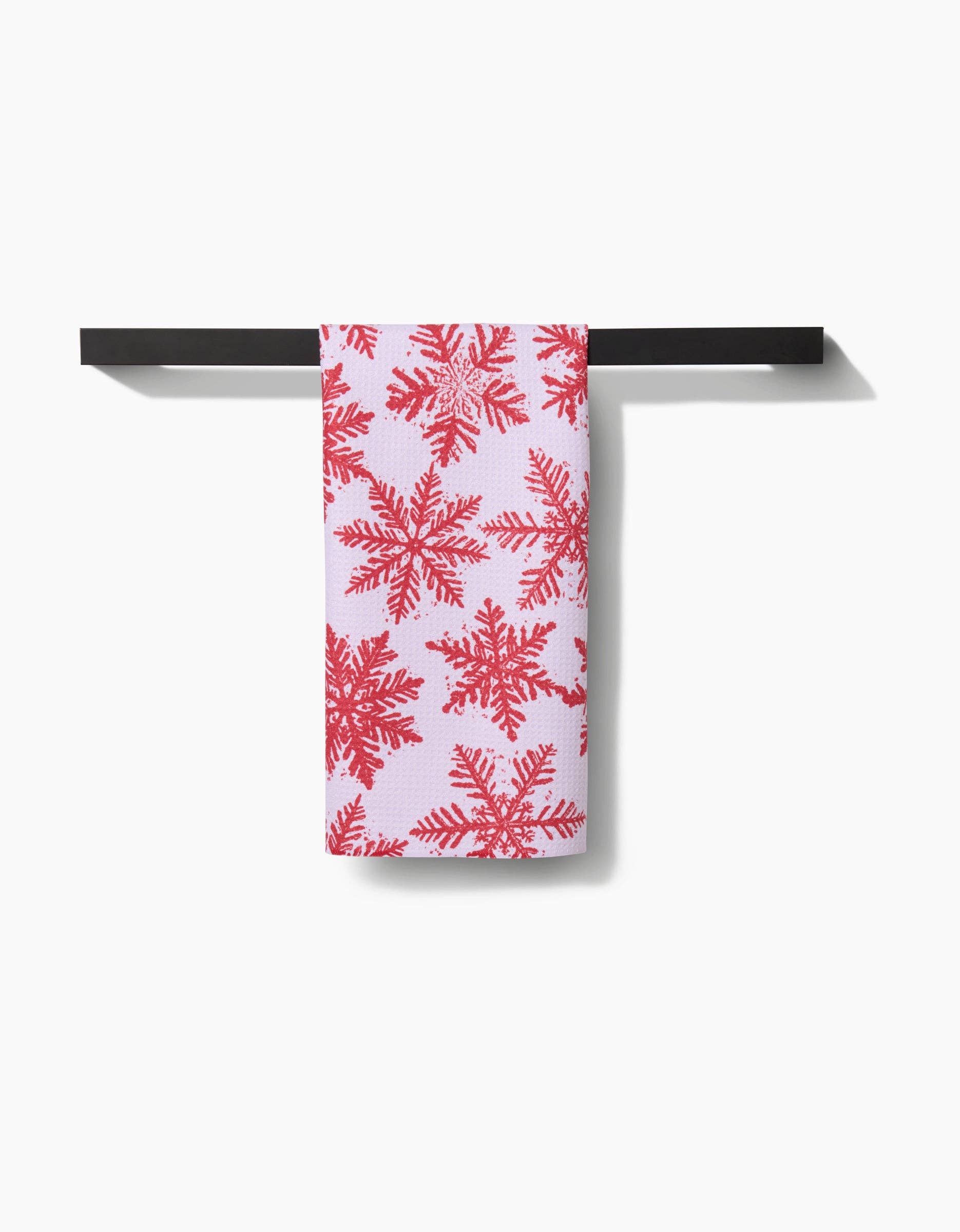 Towel with red snowflake pattern hanging on a black towel rack against a white background