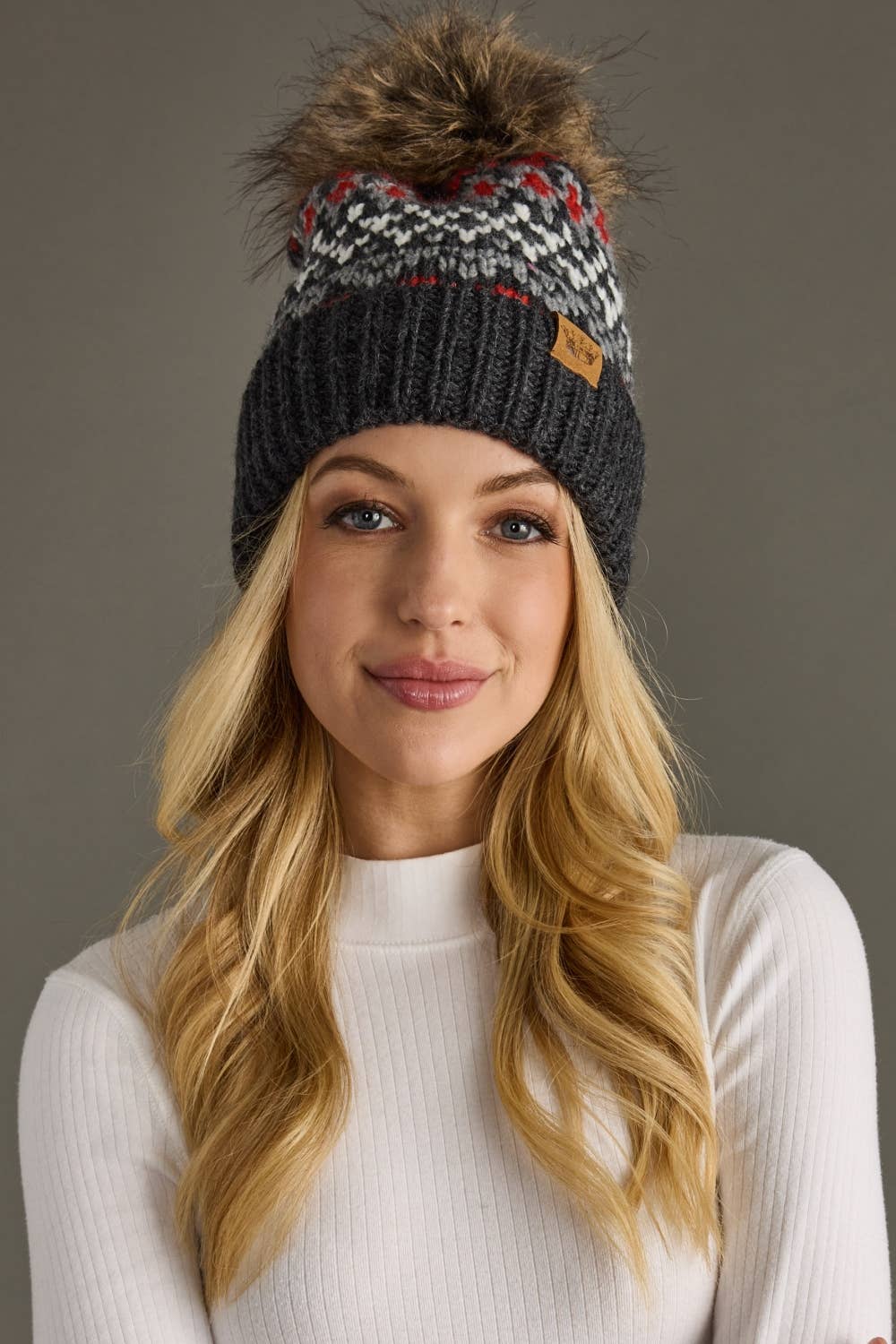 Woman wearing a patterned beanie with a pom-pom against a neutral background