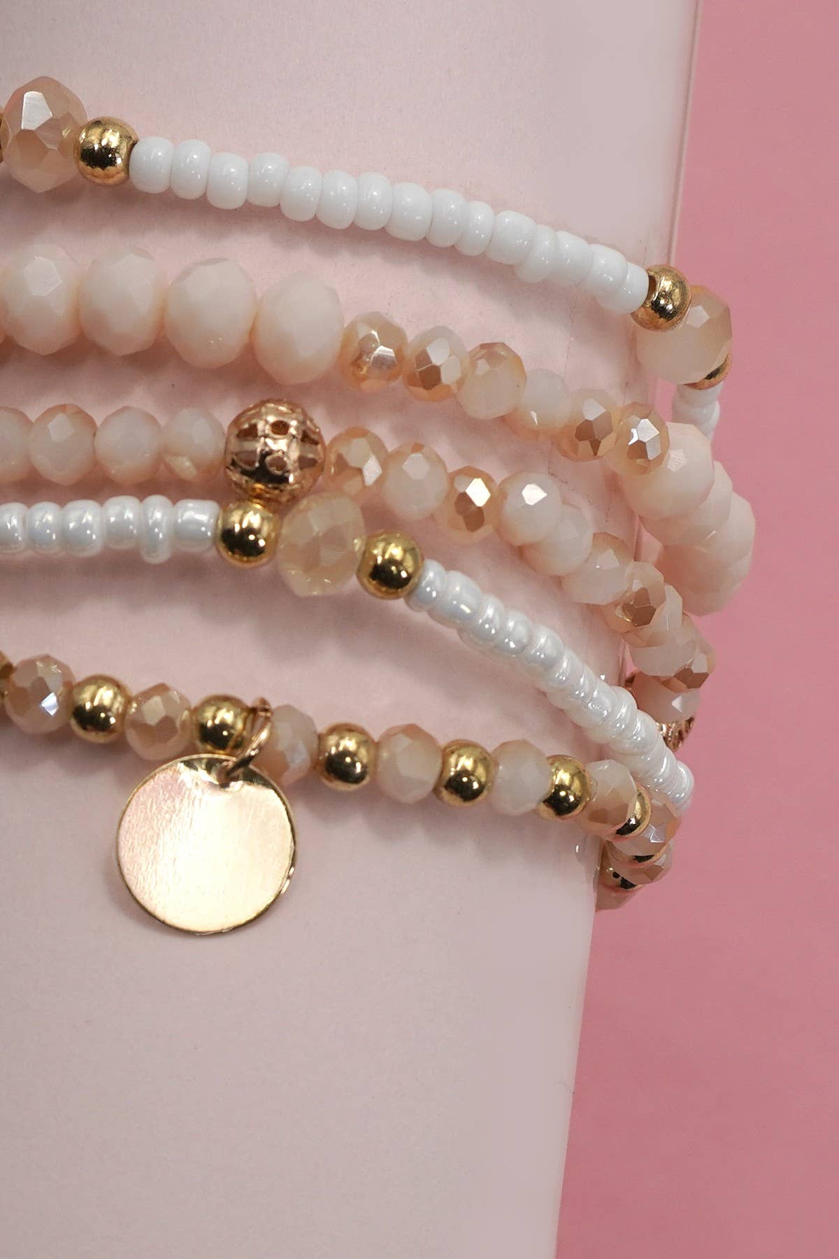 Stack of beaded bracelets with gold accents on a pink background
