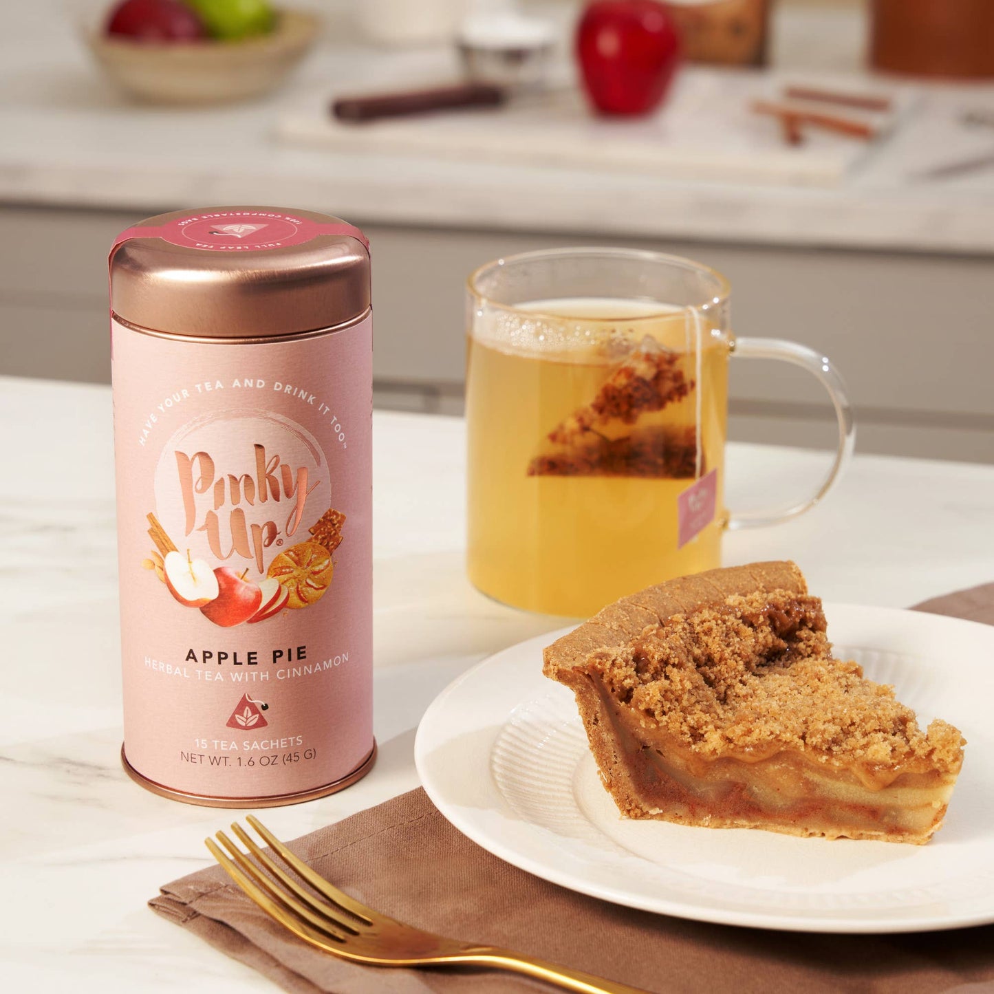Pinky Up Apple Pie tea canister with a slice of apple pie and a mug of tea on a kitchen counter.