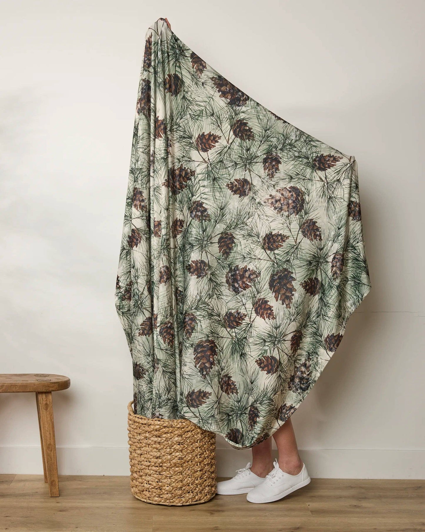 Person holding a green and brown patterned blanket over their head, standing next to a woven basket on a wooden floor Geometry Butter Blanket
