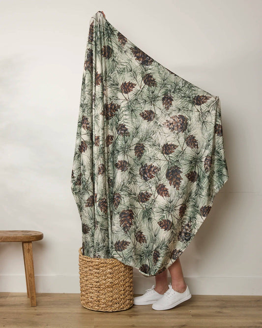 Person holding a green and brown patterned blanket over their head, standing next to a woven basket on a wooden floor Geometry Butter Blanket
