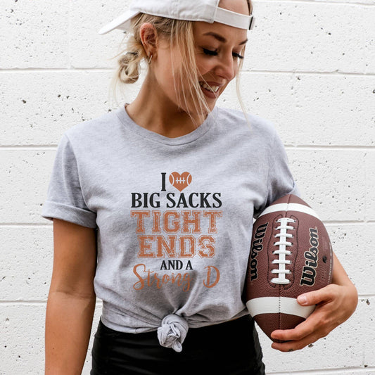 Woman wearing a t-shirt with sports-themed text, holding a Wilson football against a white brick wall.