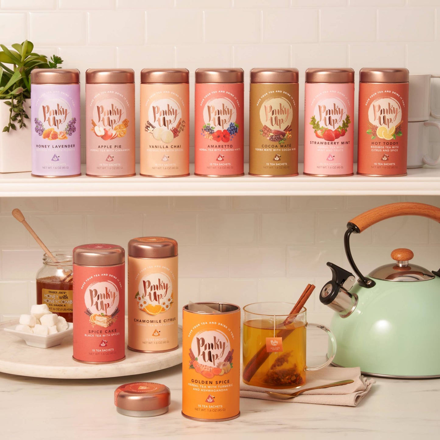 Row of 'Pinky Up' tea tins on a kitchen counter with a teacup and kettle.