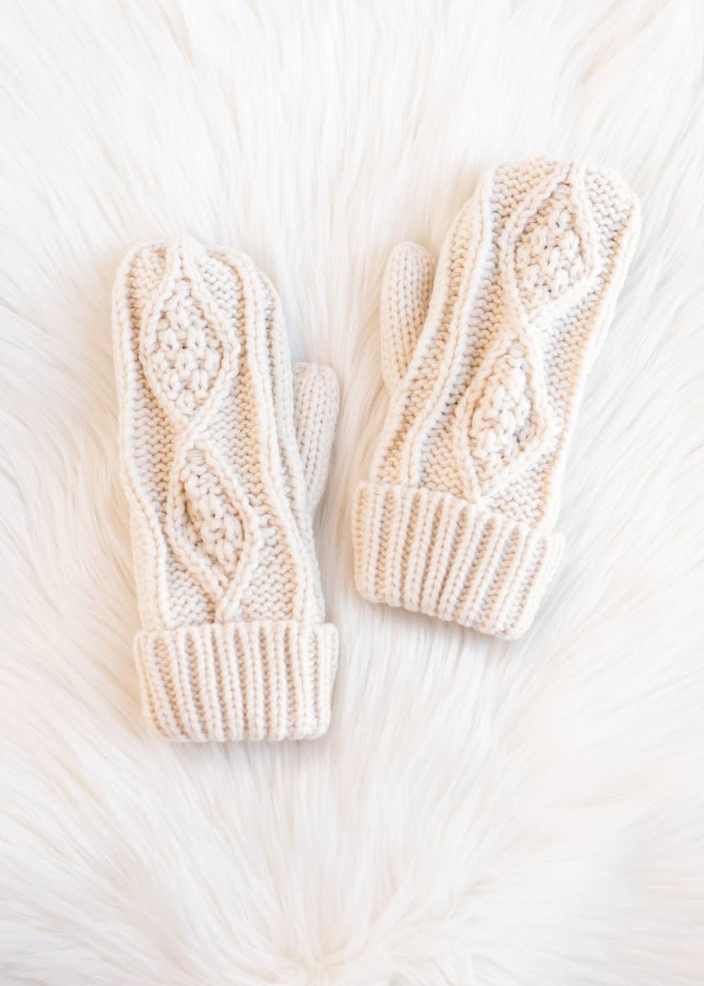 Pair of cream knitted mittens on a white fur surface