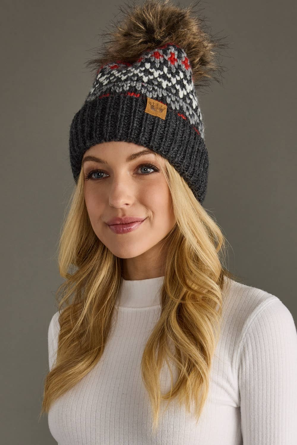 Woman wearing a patterned knit beanie with a pom-pom on a gray background