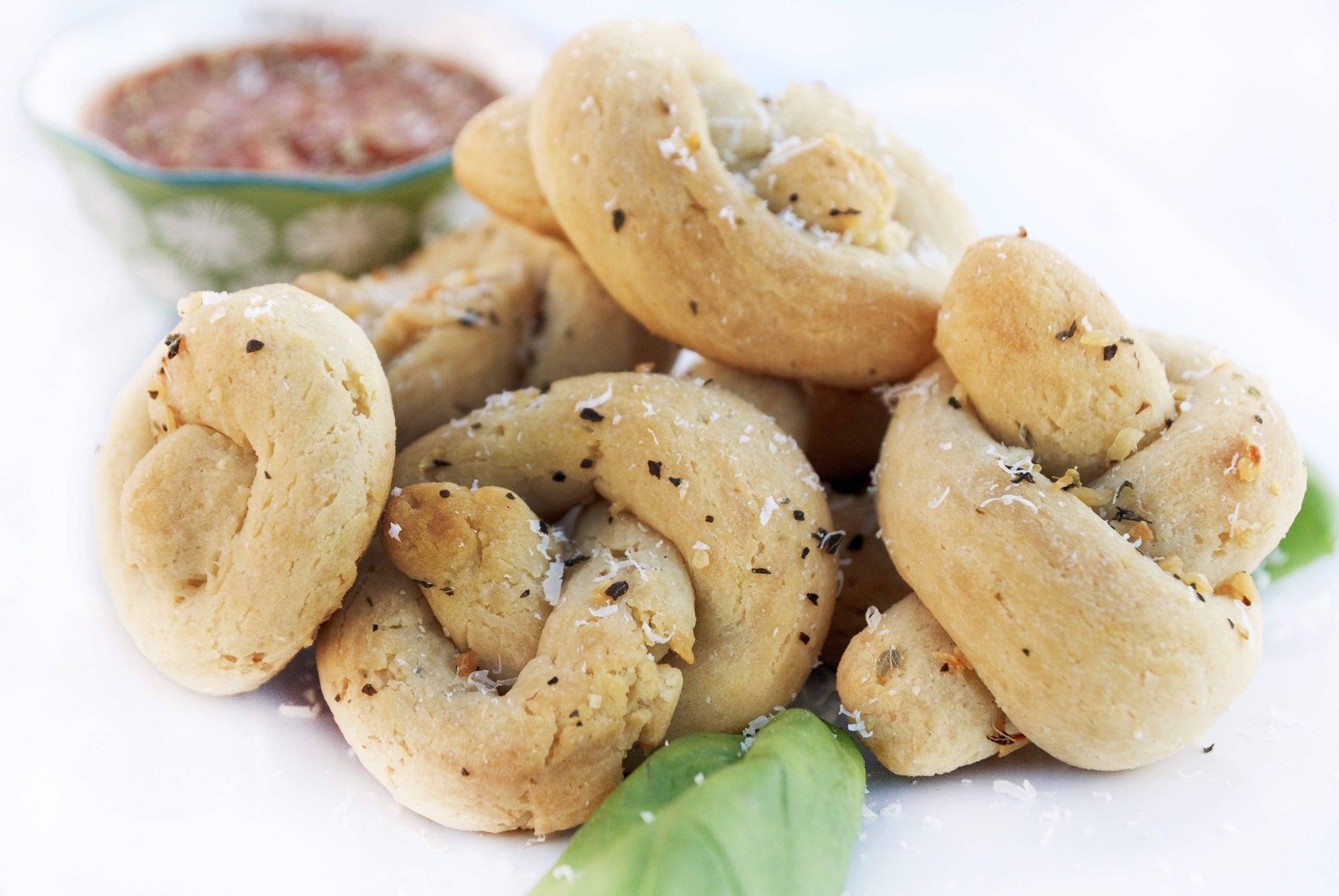 Crunchy bread rolls with herbs on a white plate with a small bowl of red sauce in the background.