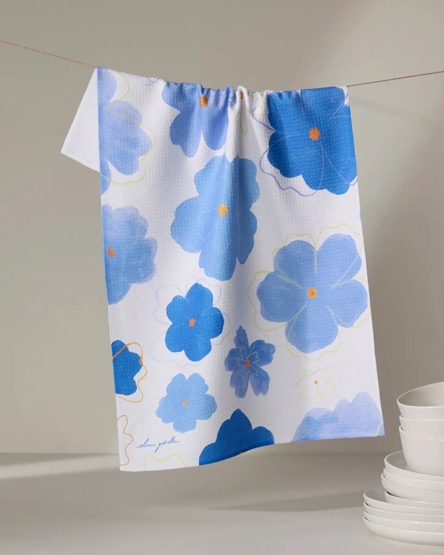 Floral Geometry tea towel with blue flowers on a white background, hanging on a line.